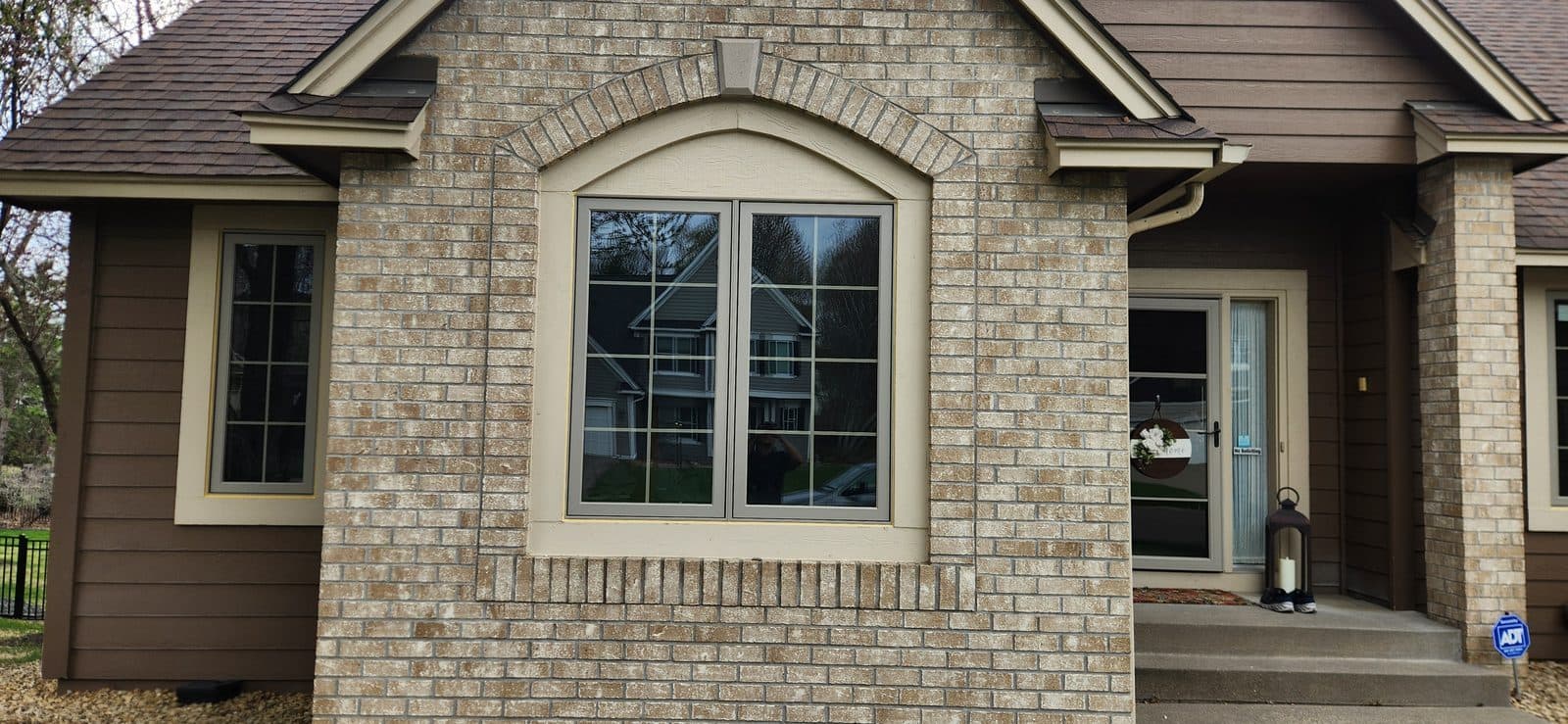 Arched-top white gridded window in a stone-veneer gable beside the front entry