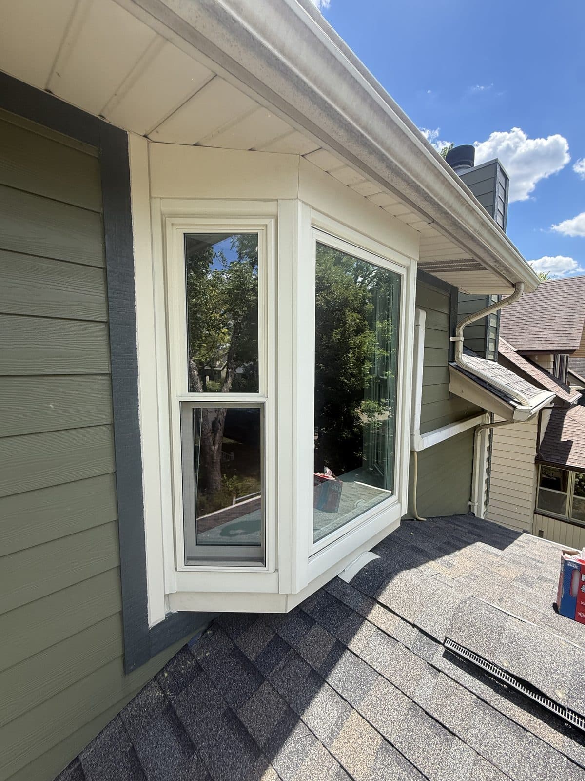Bay window exterior with its own shingled roof on a green-sided home