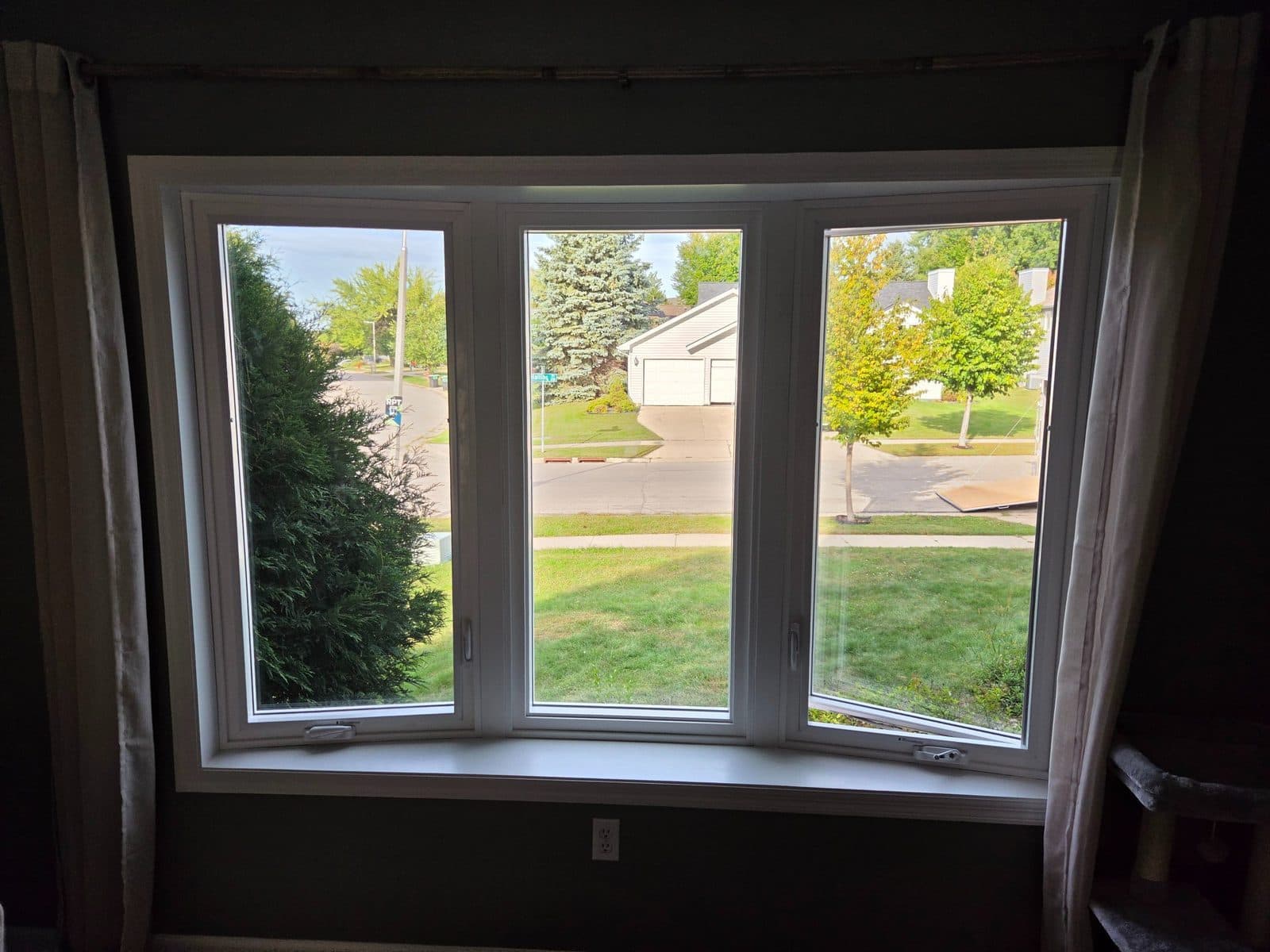 Inside of a new white bay window with curtains, street view beyond