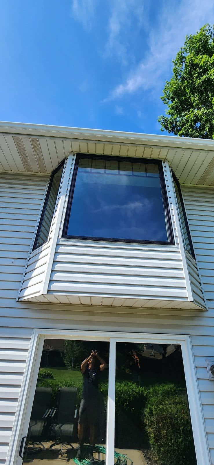 Black bay window above a new patio door on white vinyl siding