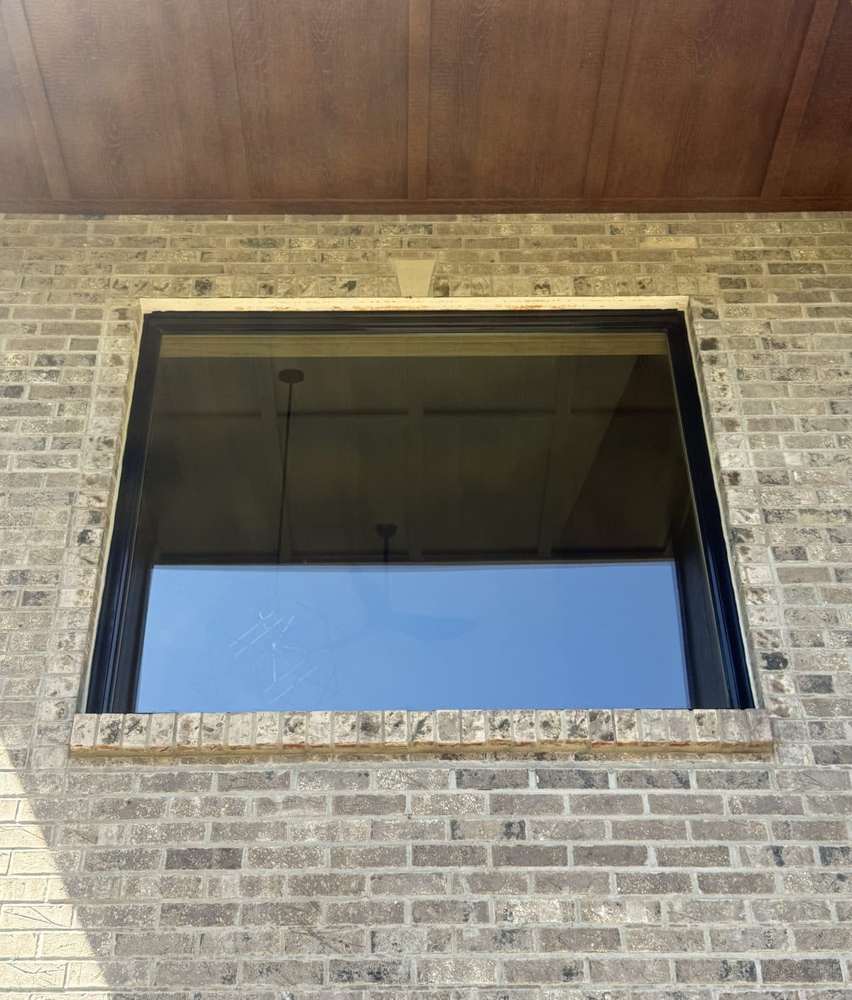 Black-framed picture window set in brick under a wood-look soffit