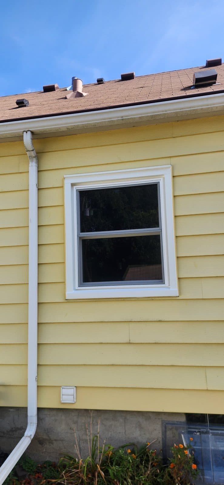New white double-hung window with capped trim under the eave of a yellow-sided home