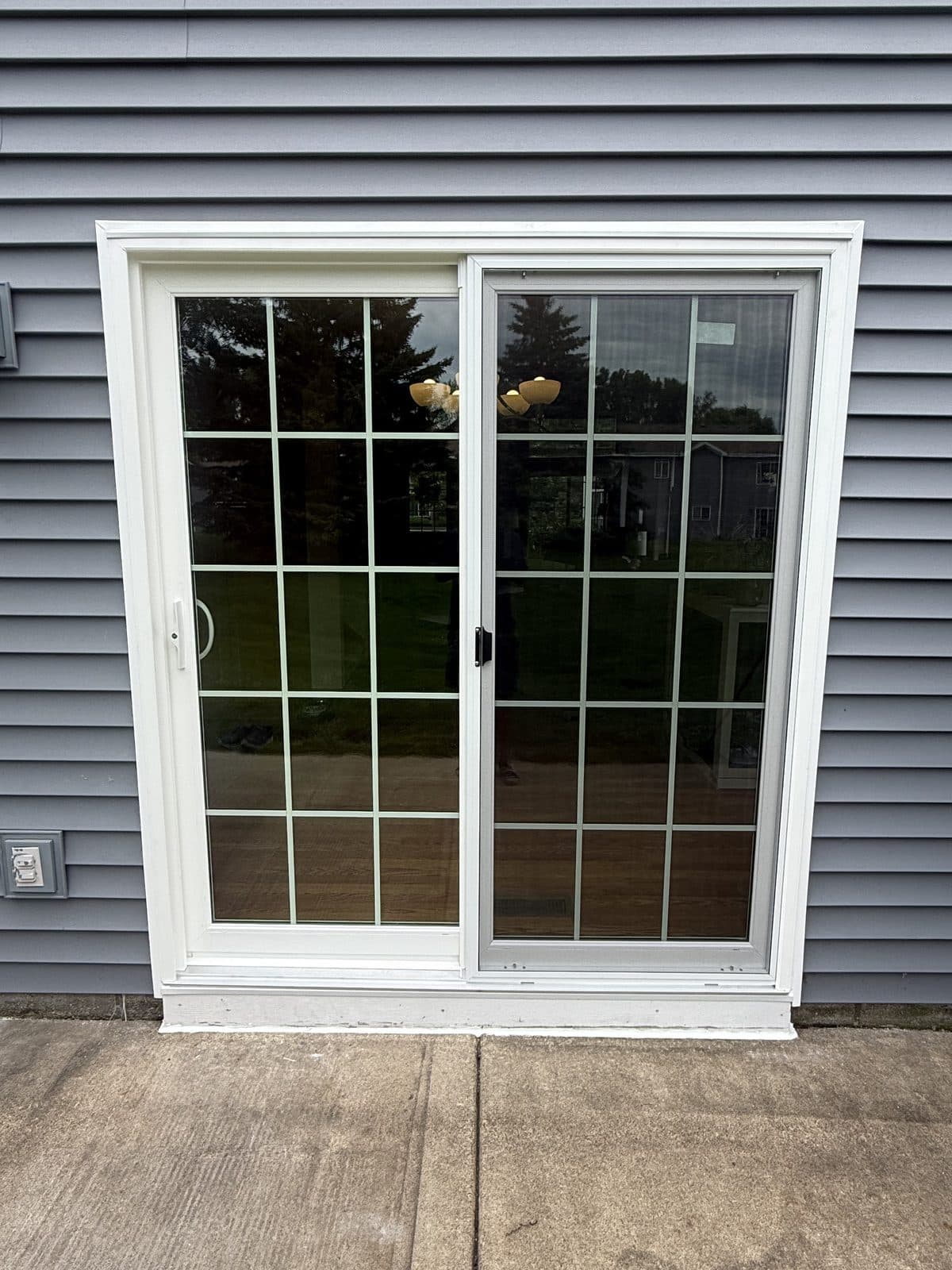 White gridded sliding patio door on dark gray siding with a clean patio slab