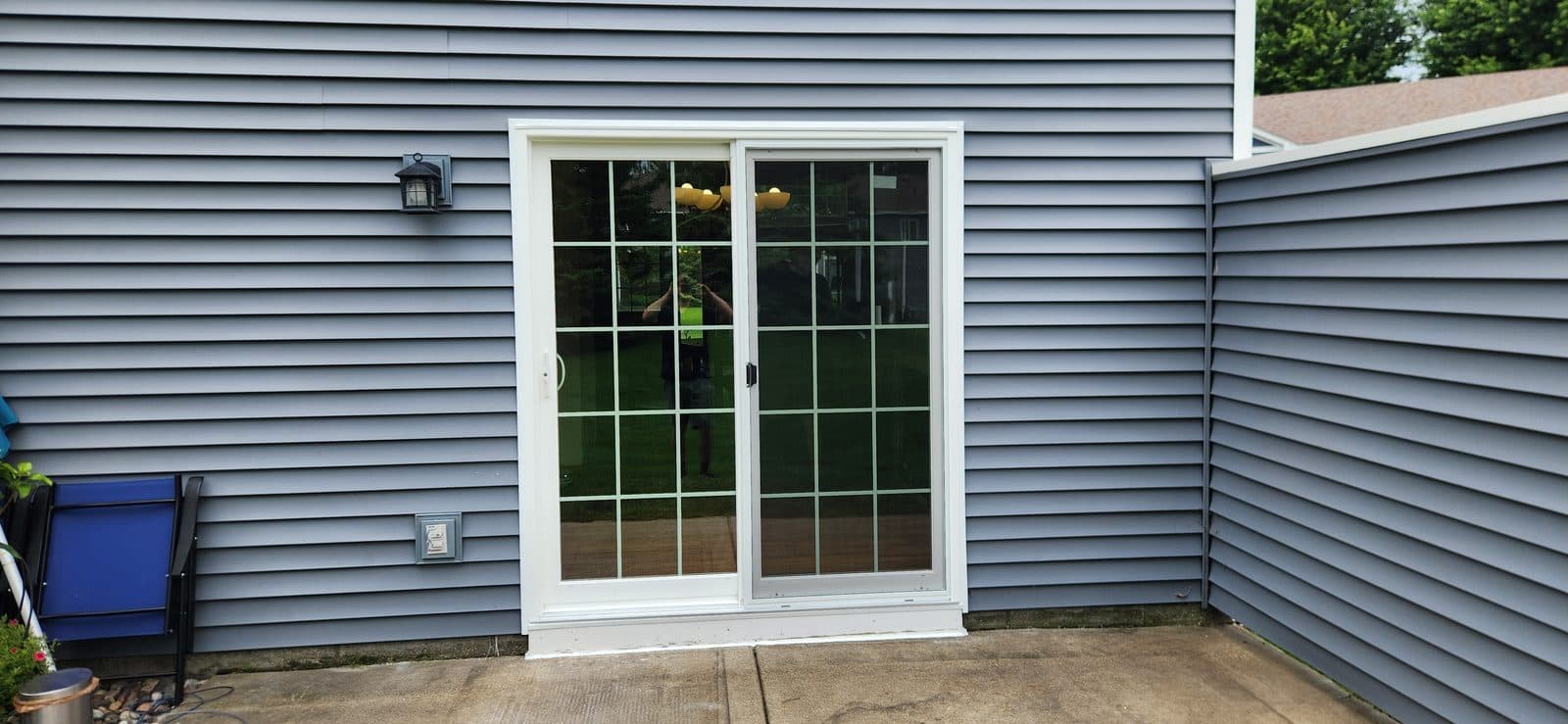 New white grid sliding patio door on gray vinyl siding with a patio