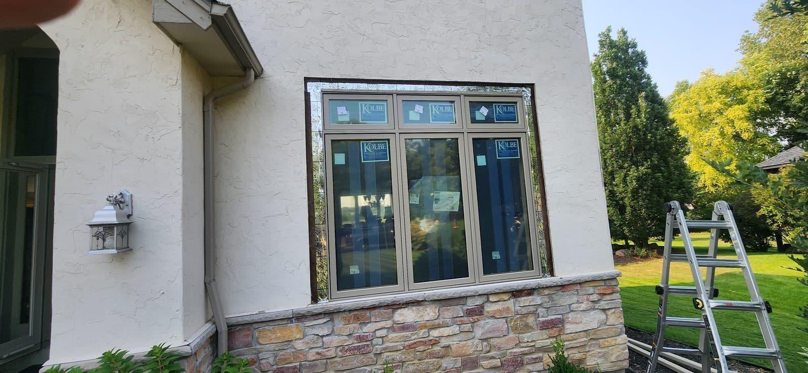 New wood casement windows being installed in a stucco and stone wall, ladder against the house