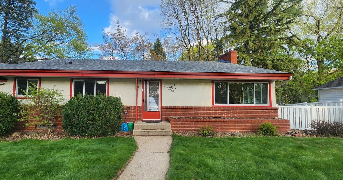 Mid-century brick rambler with new slider windows and red trim, lawn and plantings in front