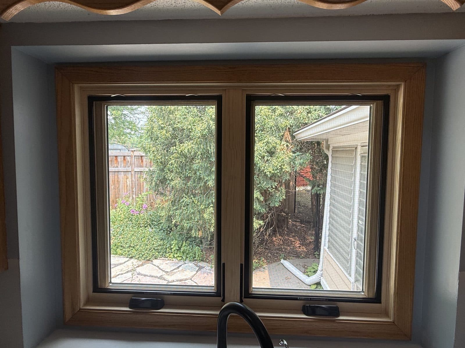 Oak-trimmed casement pair over the kitchen sink with black hardware