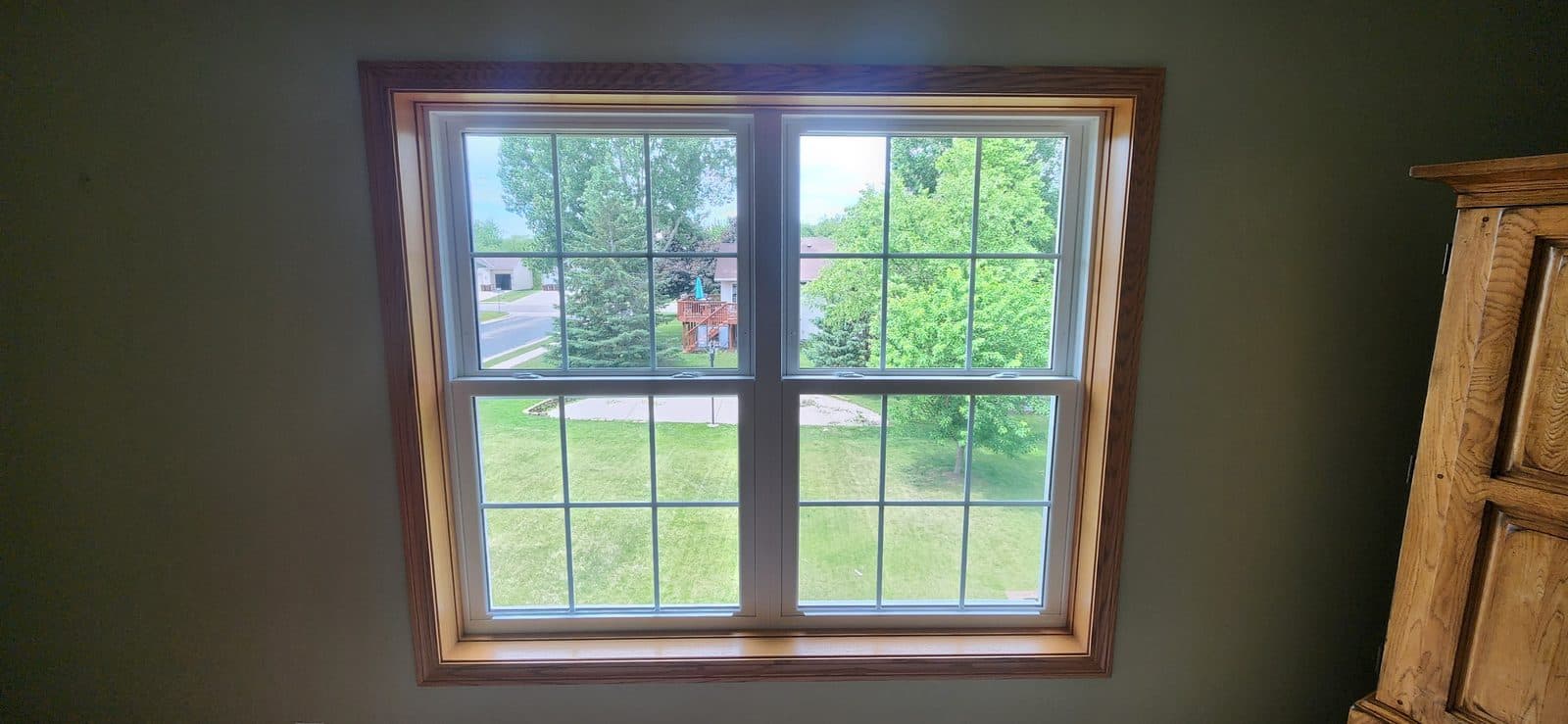 Oak-trimmed gridded double-hung pair on a green wall