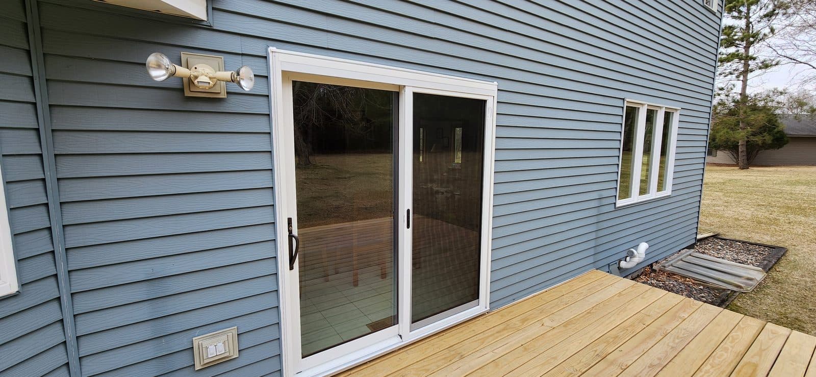 New sliding patio door and deck on a blue-sided Minnesota home at dusk