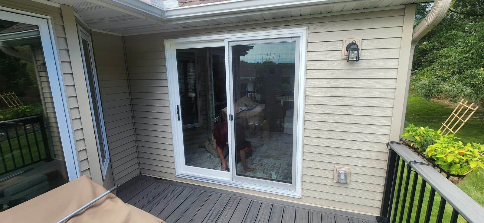 Sliding patio door with white frame seen from the deck of a cream-sided home