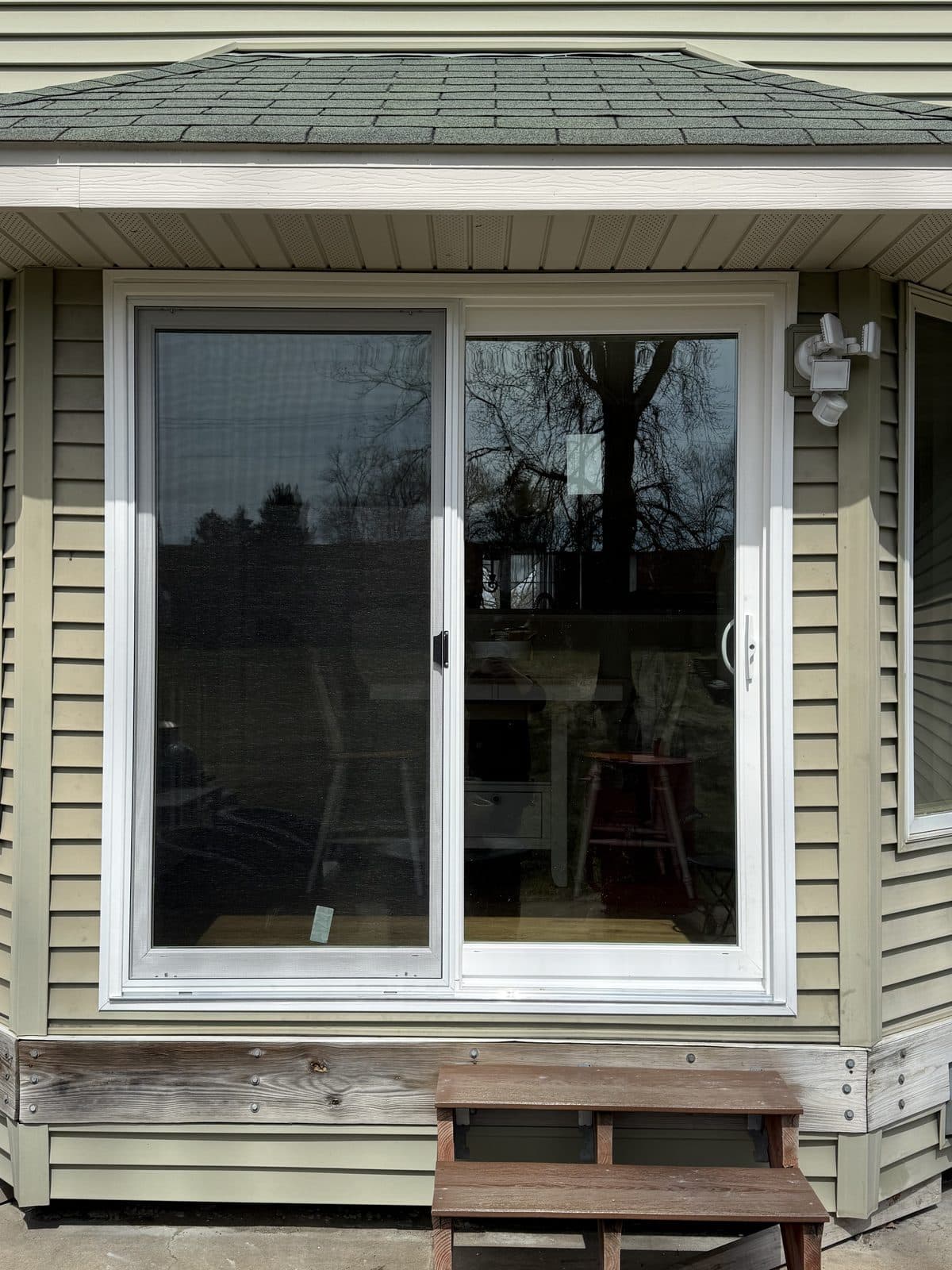 Sliding patio door with white frame on tan siding, deck steps below