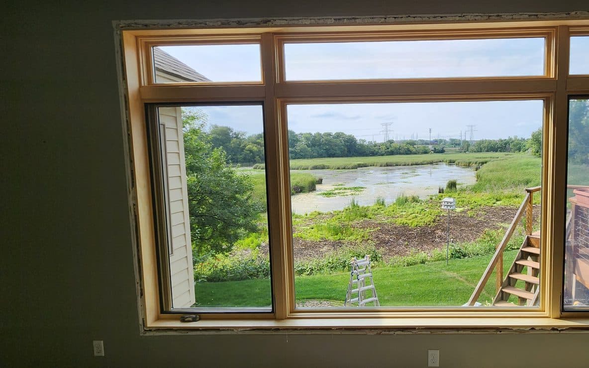 Large wood picture window with flanking casements framing a wetland view