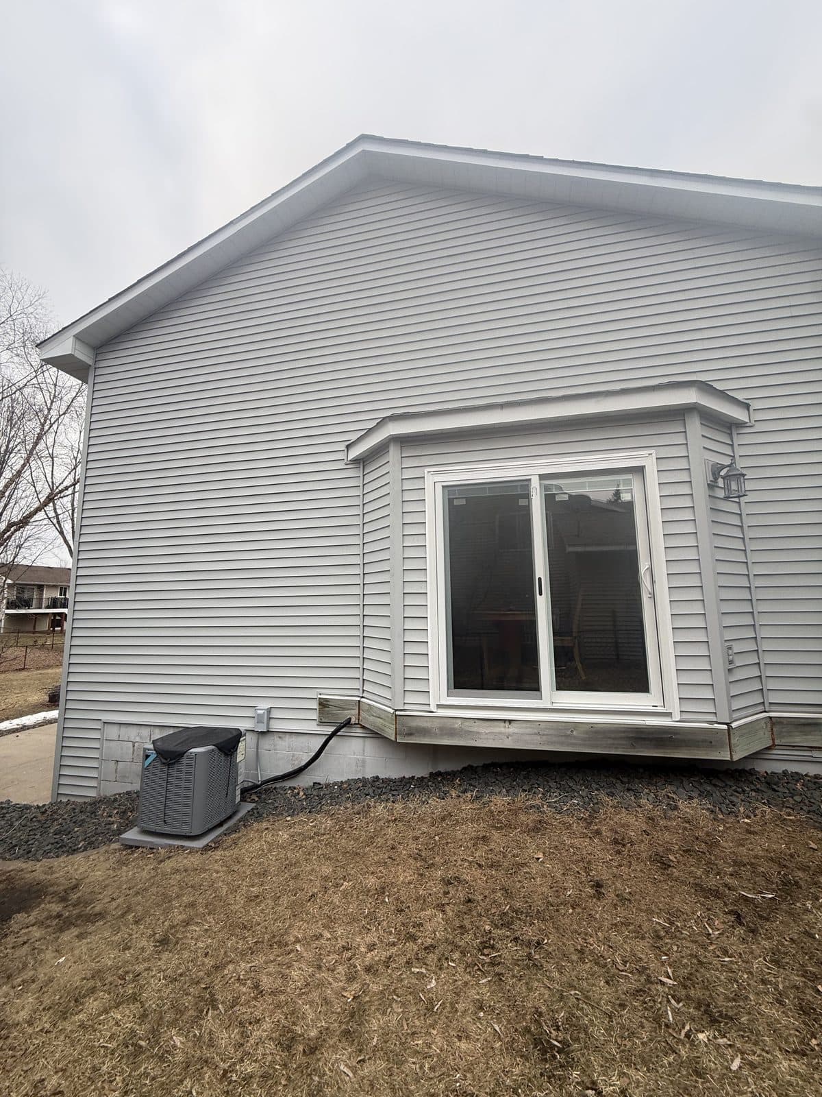Rear of a gray-sided home with a new slider window in the bump-out