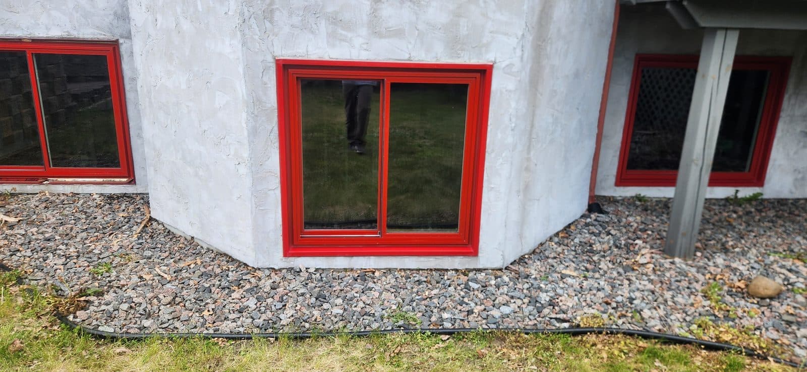 Red-framed slider windows set at grade in a white stucco wall