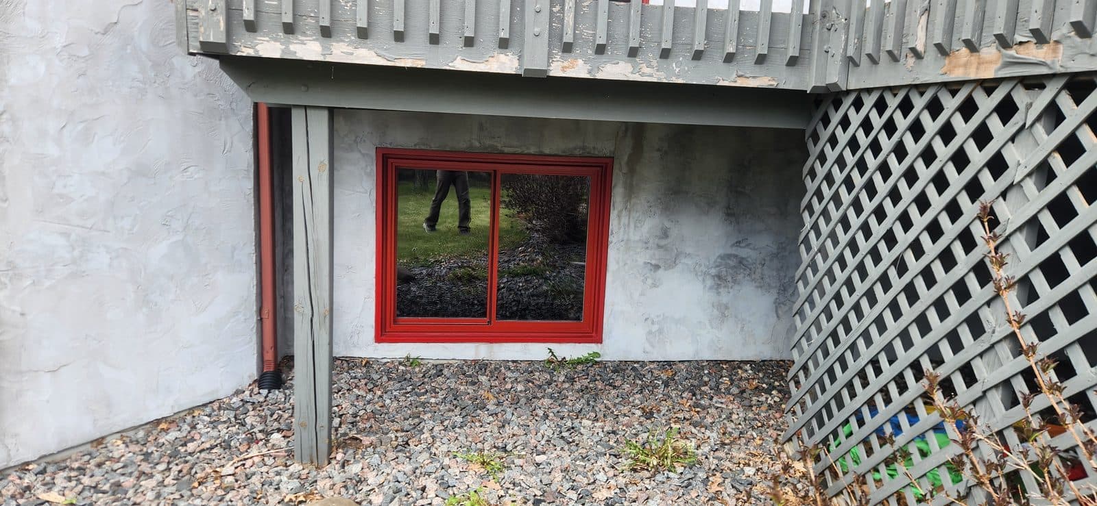 Red-framed replacement windows along a stucco walkout wall with a block retaining wall at left