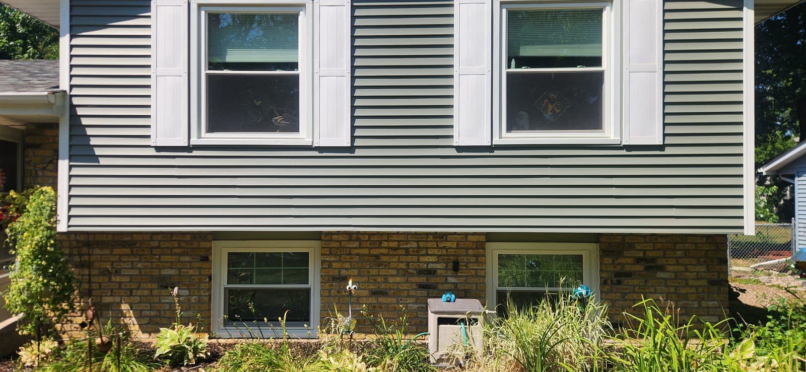 Split-level home with four new white double-hung windows set in green lap siding and brick