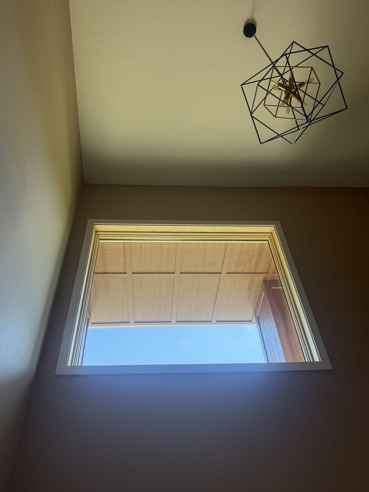 White-trimmed picture window high in a stairwell under a modern chandelier