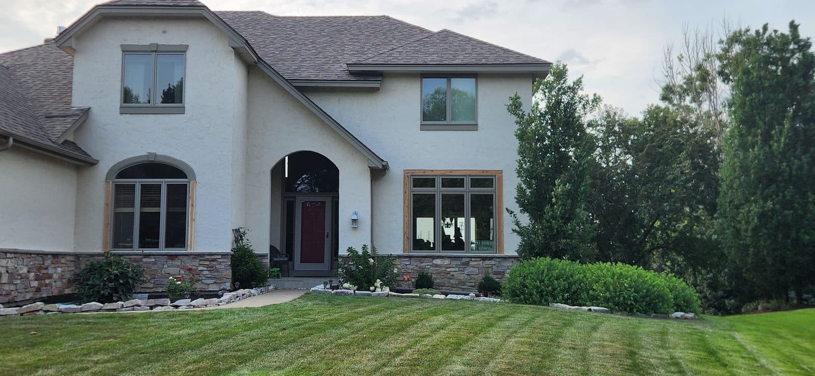 Two-story stucco and stone Minnesota home with new casement windows across the front, lawn freshly cut