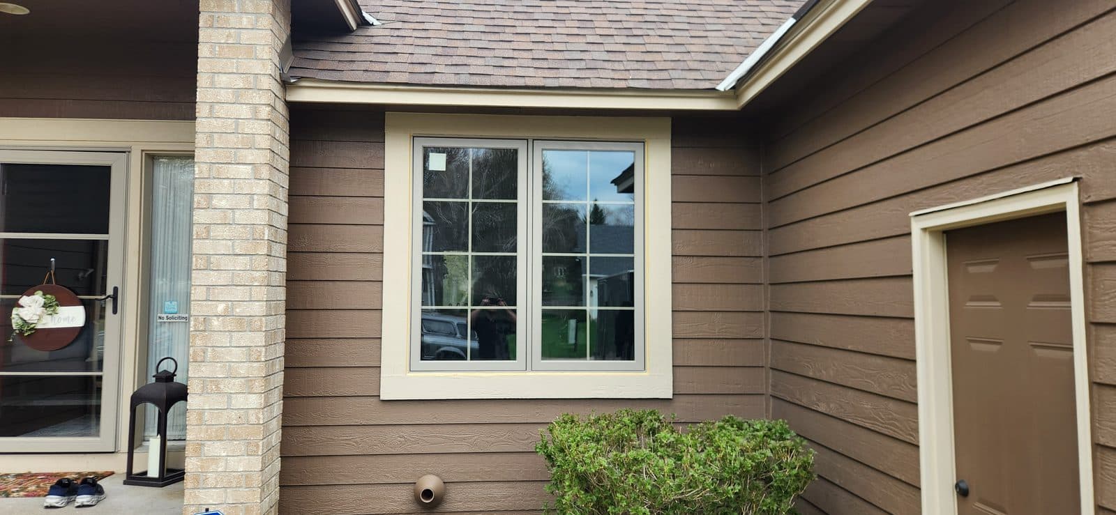 New tan double casement beside the front entry, brick column and brown lap siding