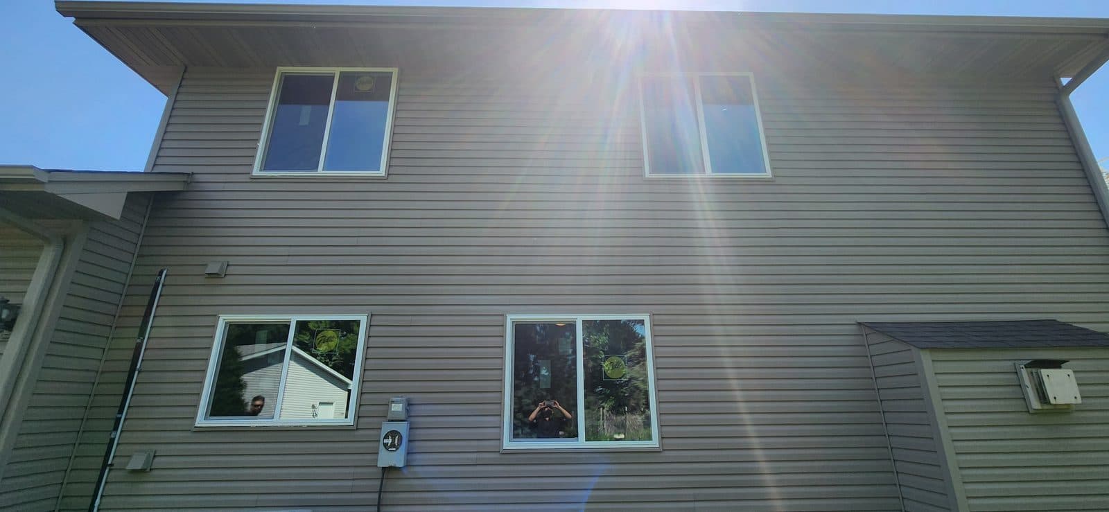 Back of a tan-sided two-story home with a full set of new white windows