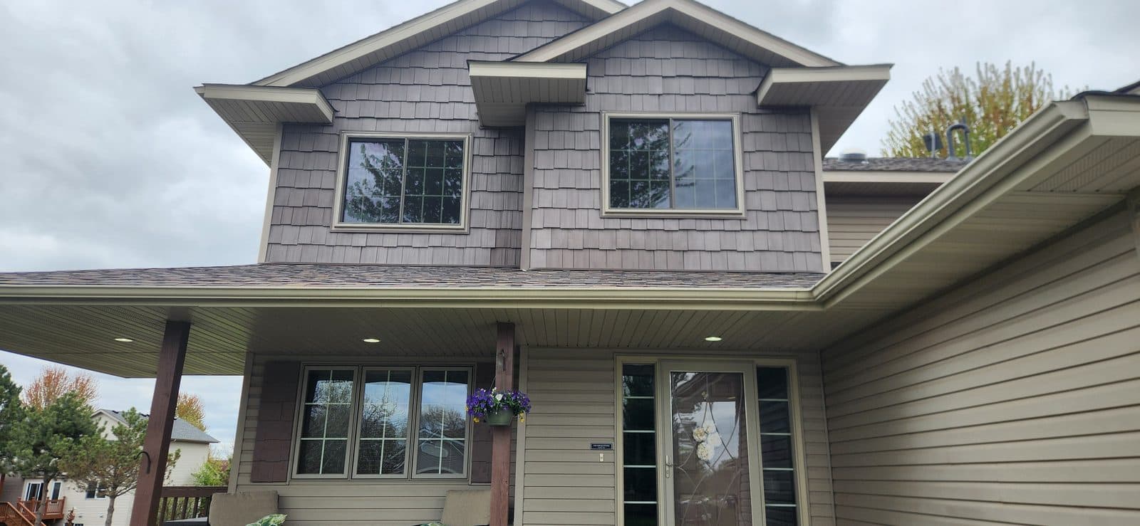 Two-story home with shake gables, new grid windows and a glass-panel entry door under a covered porch